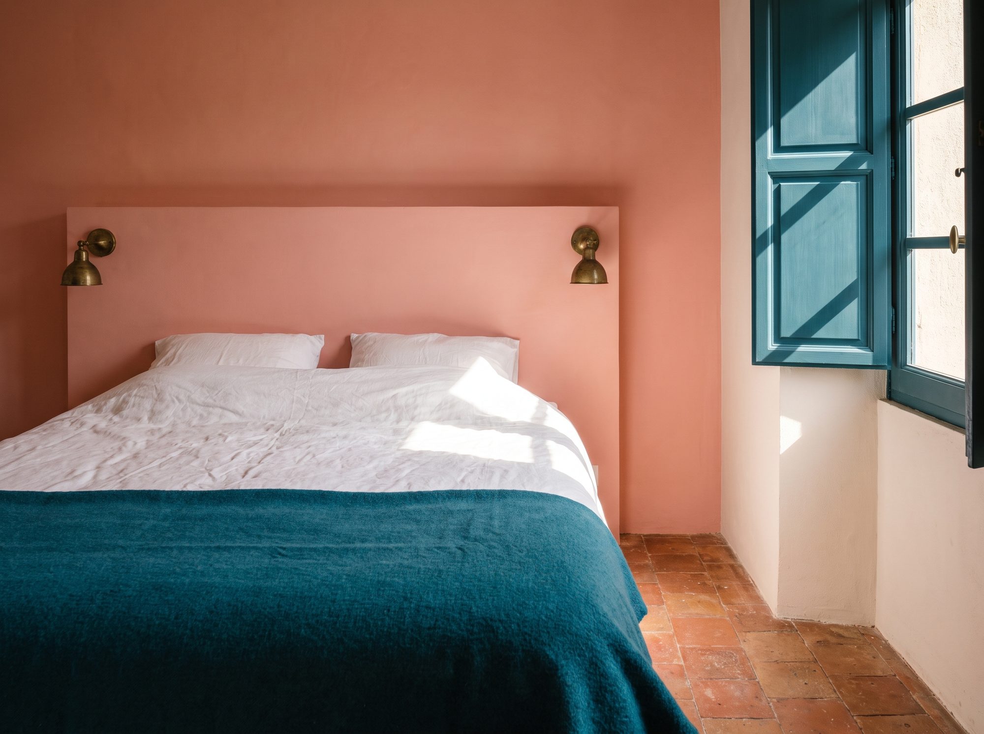 La chambre Rose : mur de chaux rose, lit en lin blanc, plaid canard, lumière dure des volets