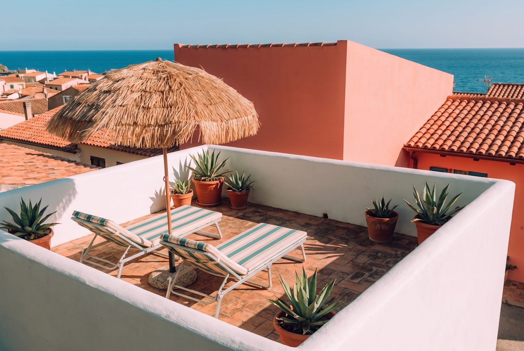 Le toit-terrasse : parapets blancs, transats rayés, parasol de paille, les toits de Collioure et la mer