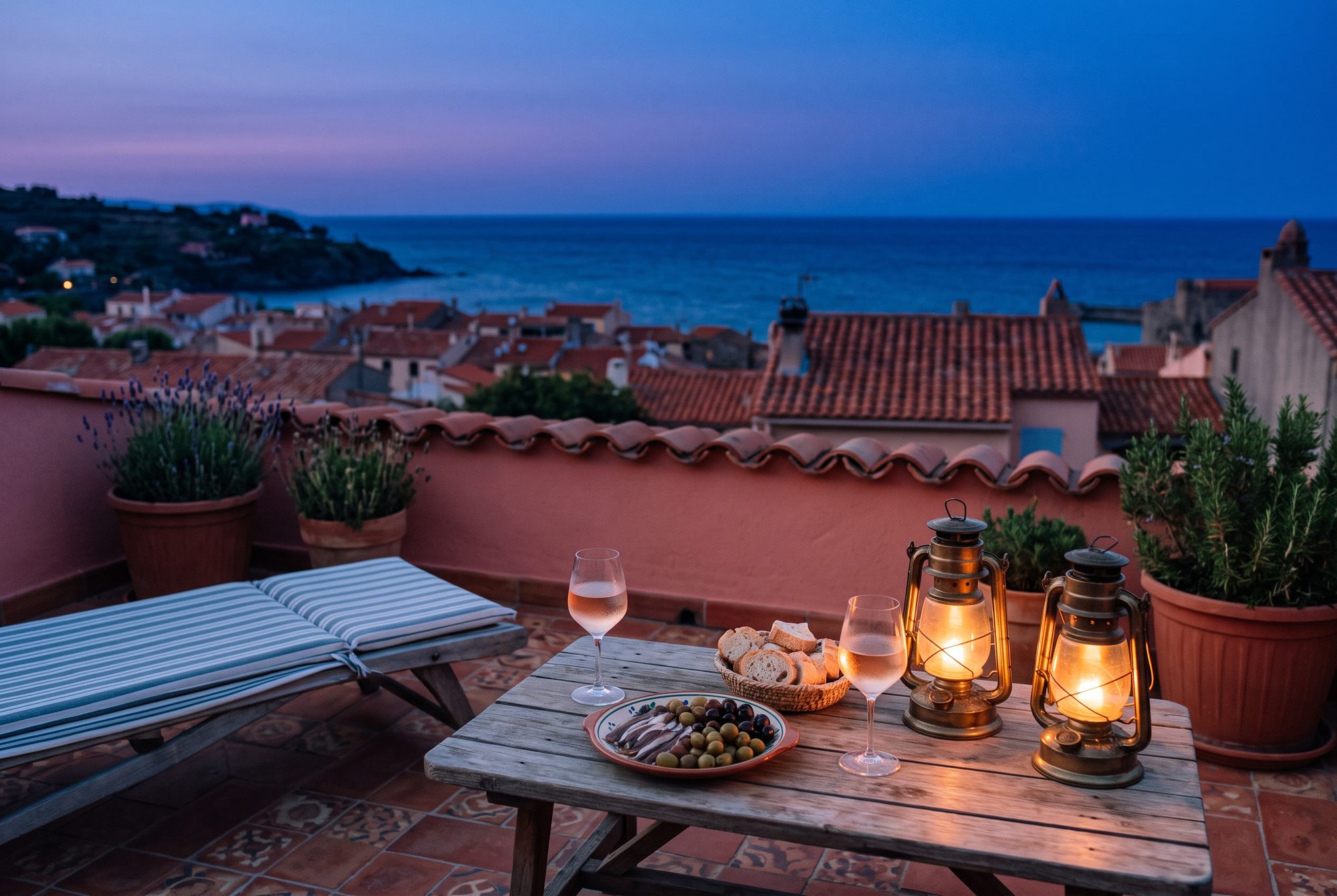 Le toit-terrasse à la nuit tombée : lanternes, verres de rosé, la baie qui s'éteint